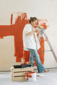 woman on phone, leaning on a ladder, with orange wall paint