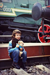 child sitting on railroad rail with teddy bear